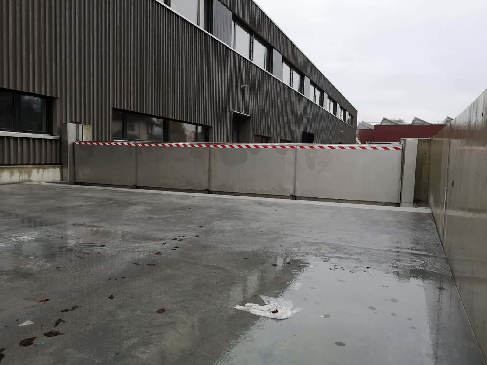 Large-scale automatic flood barrier wall protecting industrial warehouse from climate change flooding — deployed without power or staff intervention