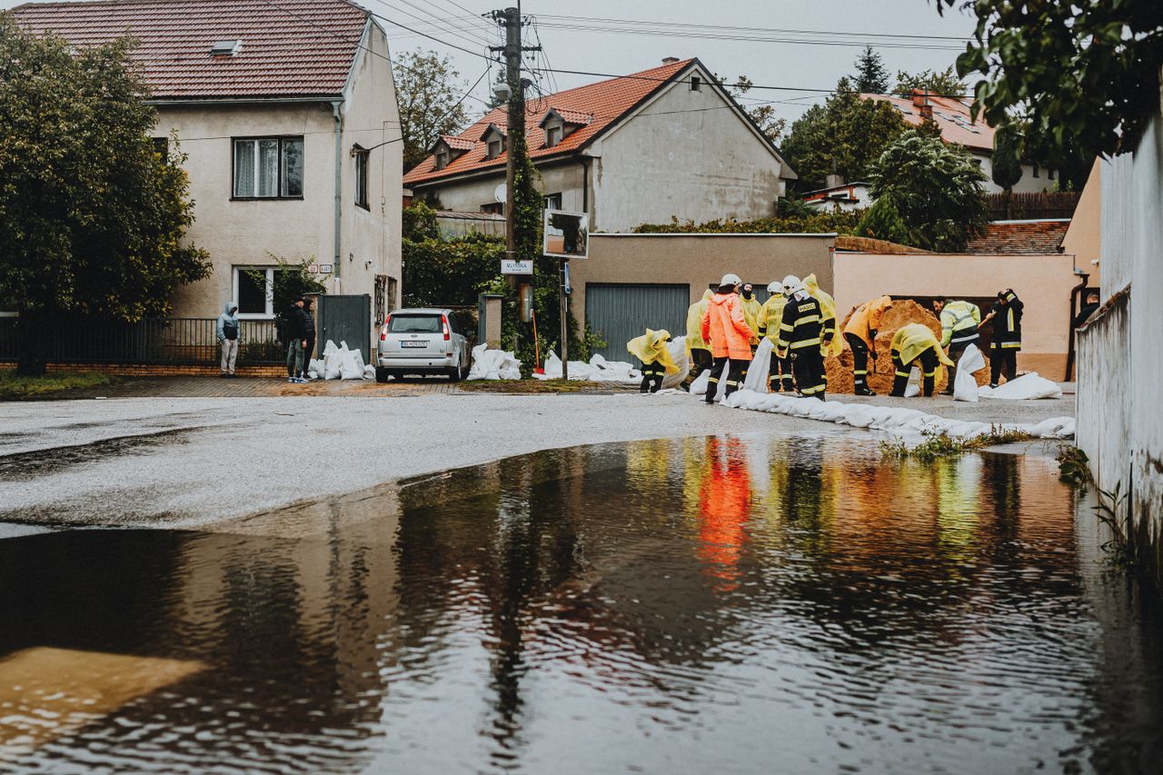 Des secouristes vêtus de tenues réfléchissantes interviennent face aux inondations dans une rue résidentielle.